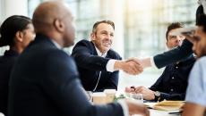 Two people shake hands in a meeting at a table